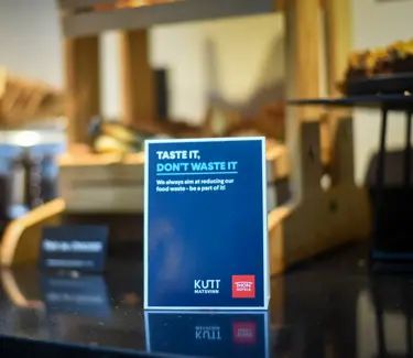 Skilt med teksten "Taste it, don't waste it" på et buffetbord, der fremmer madspildsreduktion.